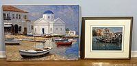 Two George Bates art prints displayed side by side against a wall on floor, one with a wood frame and matting showing a Venice canal scene, the other larger print on wood board depicting Mykonos white buildings and boats.
