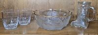 Photo showing clear glass short tumblers, frosted glass bowl with gold trim, and glass boot-shaped mug on wooden shelf