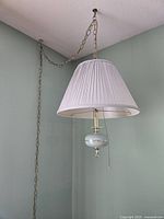 Side view of hanging light with white pleated lampshade, brass accents, and ceiling chain mount.