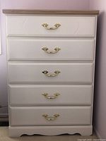 Front view of a 5 drawer high boy dresser, showing white drawers with gold handles and a light wood top.