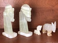 Pair of carved marble Trojan horse head bookends with visible natural striations and small chip on ear; two small carved animal figurines, donkey and unicorn, beside them on wooden surface