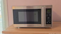 Microwave full frontal view on wooden surface with closed door, showing stainless steel finish and window.