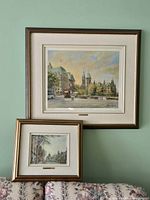 Two framed Ottawa prints hanging on wall showing Confederation Square and Wellington Street scenes. Both are in bronze tone frames with cream mats and plaques.