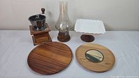 Overall lot showing coffee grinder, candle lamp, porcelain dish, and two wooden plates on white surface