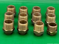 Photo showing all 12 brass hex nipple fittings arranged on green background, clearly showing threaded ends and hex shape.
