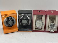 Four watches, two black Champion brand sports watches with digital displays and two silver metal band watches in display boxes