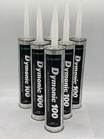 Front view of 5 Tremco Dymonic 100 sealant tubes standing upright with white applicator nozzles attached on top, visible product labels and branding.