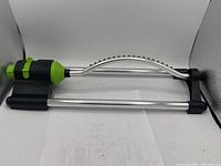 Photo of ProYard oscillating sprinkler showing metal frame, green and black fittings, and curved spray bar with 18 jets.