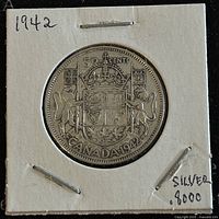 Obverse of the coin showing the Canadian coat of arms, denomination 50 cents, and year 1942. Mounted in a white paper holder with handwritten notes indicating silver content and year.