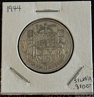 Front side of 1944 Canadian 50 cents coin showing the Canadian coat of arms with shields, crown, lion, unicorn, and maple leaves, secured in a paper holder with handwritten 1944 and silver content notes.