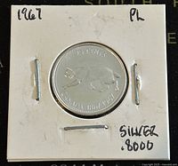 Front side of the 1967 Canadian 25 cents coin showing a polar bear and years 1858/1958 with inscription 'Canada' and '25 cents.' Coin is secured in a white cardboard holder with handwritten notes.