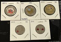Photo of 3 toonies dated 2021 and 2022, each with coloured décor markings and in white holders