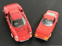 Two red Ferrari die cast model cars, 1964 Ferrari 250 LM and Ferrari 365 GTB4 Daytona, shown from above on a black surface.