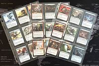27 Magic The Gathering collectible trading cards in sleeves, spread out on world map background, showing front artwork and text