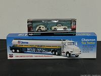 Maisto 1966 Volkswagen Karmann Ghia and traveler trailer boxed set displayed on top of Chevron 1999 limited edition toy tanker truck box, showing full packaging and scale details.