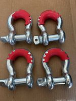 Four metal D rings with partial red coating on the curved part, lying on cardboard