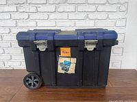 Front view of black and blue rolling toolbox showing wheels and locking clasps.