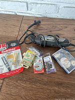 Photo showing the Dremel 4300 rotary tool along with JB Weld KwikWeld epoxy, sanding bands, cutting wheels, and accessories on a wooden surface.