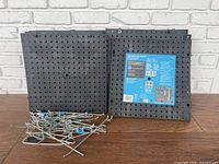 Front view of multiple black Everbilt pegboards stacked together with many metal hooks placed in front on a wooden surface.