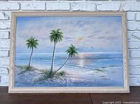 Full view of the framed beach scene painting showing three palm trees, ocean, and sunset.