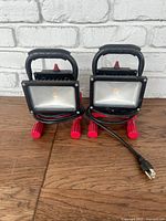 Pair of Husky high intensity LED floor lights with black frames and red legs, plugged power cords visible.