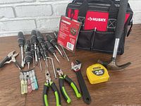 Husky tool bag with screwdrivers, pliers, adjustable wrench, hammer, Vice grips, and Stanley tape measure displayed on wooden surface.