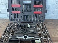 Open black plastic molded case containing assorted taps in the lid, dies and threading tools in the base.