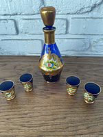Full view of decanter with stopper and four matching glasses on wooden surface in front of grey brick wall.
