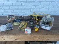 Mixed mechanic and handyman tools spread on a table including plastic bin with accessories and Central Pneumatic paint sprayer.