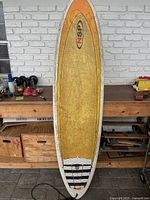 Full length photo of yellow NSP surfboard showing overall wear and wax buildup on top deck with leash attached at tail.