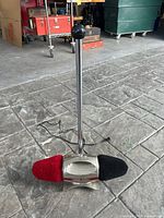 Floor setup of the vintage electric shoe polisher showing chrome body with red and black brushes and the tall chrome pole with a black knob.