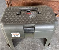 Black Rubbermaid step toolbox with handle and latch, top view showing textured surface and label.