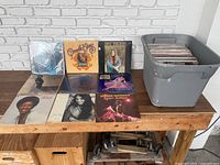 Photo of displayed vinyl albums and plastic bin containing additional albums on wooden table