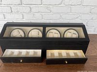 Full front view of black watch winder box with clear glass top showing 8 winding positions and two lower drawers open with 4 separate storage slots each.
