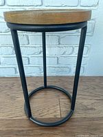 Side view of the side table showing the black metal frame and round wooden top.