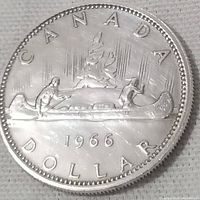 Reverse side of the 1966 Canadian silver dollar coin featuring two Indigenous people in a canoe, trees, and the year 1966.