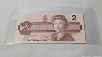 Full view of 1986 Canadian 2 dollar bill inside a plastic protective sleeve on white background.