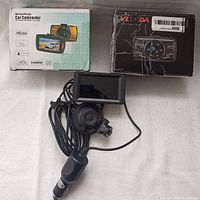 Photo of loose dashcam with screen, suction mount, charger cable next to two boxed dashcams in factory packaging.