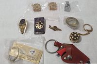 Photo showing a collection of pins and keychains laid out on a white surface including Toronto Maple Leafs pins, an Olympic pin, keychains with watch faces, miniature tools, and decorative pendants.