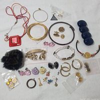 Photo showing a large assortment of costume jewelry items including necklaces, bracelets, earrings, pins, and a fur pom-pom brooch, arranged flat on a white surface.