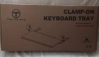 Front view of the sealed factory box with product name, brand Tech Orbits, and illustration of the keyboard tray showing clamp attachments and flat tray surface.