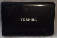 Closed black Toshiba laptop lid with brand logo on top surface, showing scratches and wear.