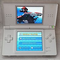 Front view of white Nintendo DS Lite turned on playing Mario Kart DS game showing gameplay menu on dual screens.