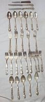 Full layout of 28 silver plated cutlery pieces: forks, spoons, and knives with decorative handles.