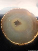 Top-down photo showing the agate slice with translucent layered banding and a crystalline center cavity, situated against a neutral background.