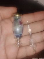 Close-up of the antique glass perfume bottle held in hand showing bulbous body with subtle color patterns, clear glass rims with gold tint, and separated delicate glass stopper with detailed spiral design.