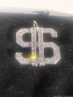 Close up of silver plated dollar sign pendant set with clear CZ stones on black background