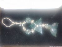 Photo of large green triangular and whale tail shaped pendant, wire wrapped with beads, laid out flat against a black background.