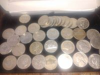 Photo showing a large assortment of Canadian and US nickels laid out on a black surface and partially inside a white box.