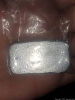 Photo of a rectangular pewter ingot showing textured surface and matte silver color held in a hand for scale.